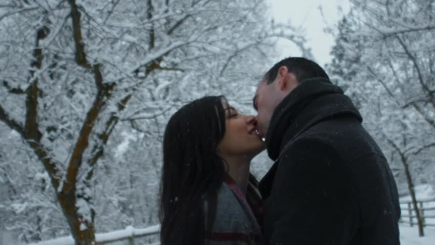 Man and woman kiss outside while snow falls