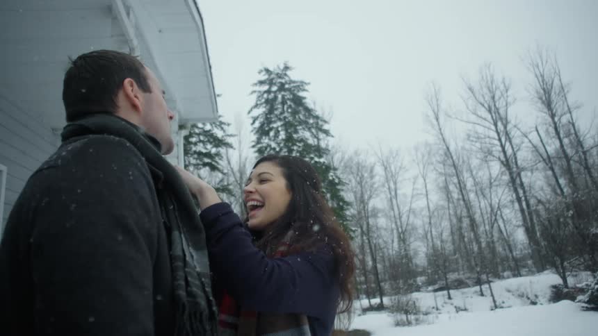 A woman adjusts a man's scarf in the snow