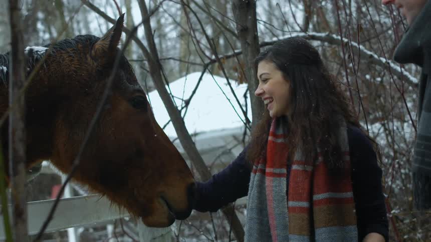 Woman smiling as she pets a horse while snow falls