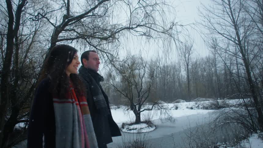 A man and woman walk as snow falls