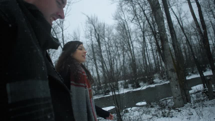 Two people are walking near a stream as it snows