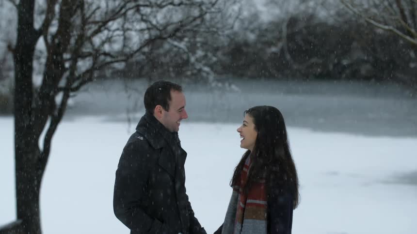 A man and woman stand in a snow-covered area laughing and talking