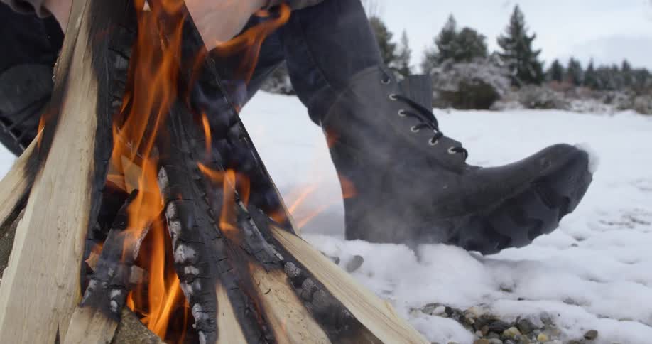 A man sits in the snow next to a fire