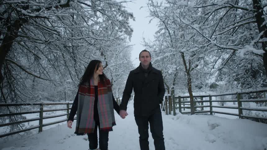 A man and women hold hands and walk down a snow covered trail