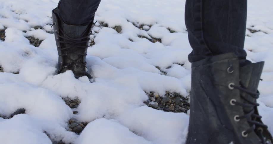 A person in black snow boots trudging through the snow
