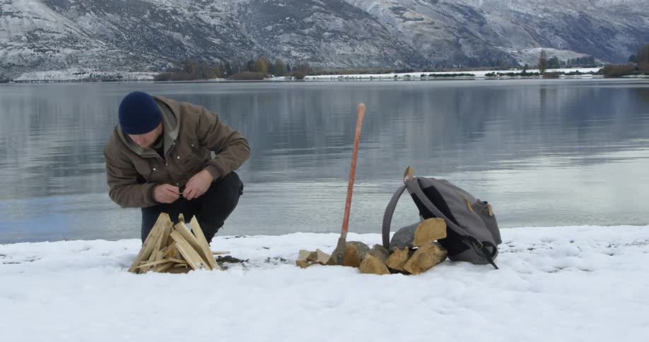 Man kneeling in snow trying to start a fire