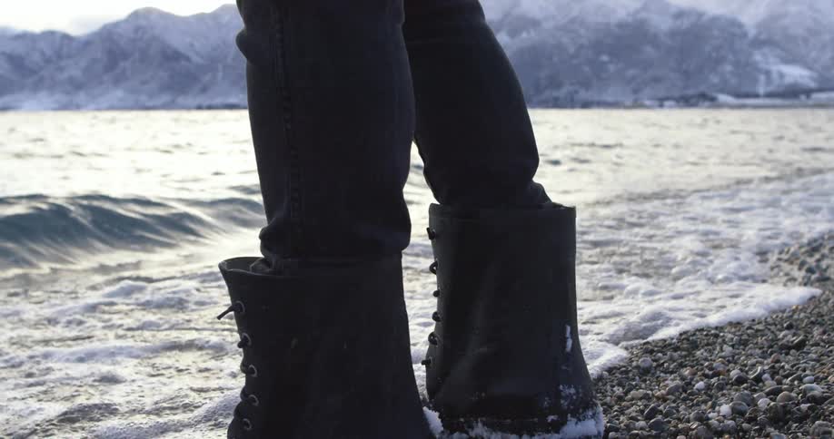 Person walks to the shore and stands as the water hits