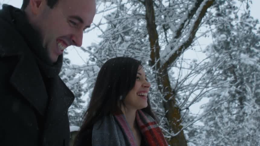 A man and woman walking are laughing while a light snow falls