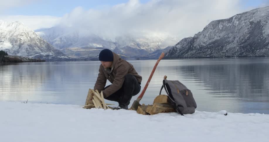 Man crouched by the water trying to start a fire