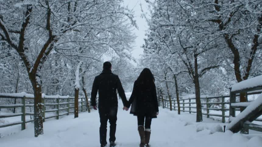 A man and woman hold hands as they walk down a snowy lane