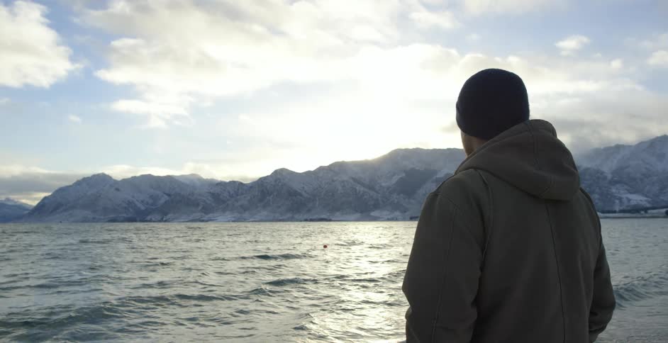 Man standing and overlooking a large body of water on a cloudy day