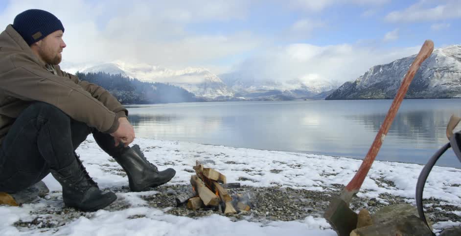 Man sits next to a fire by the water