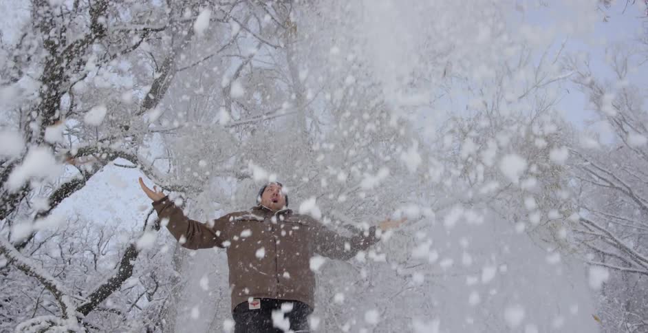 Man walks in a forest and pulls a branch down to release snow everywhere
