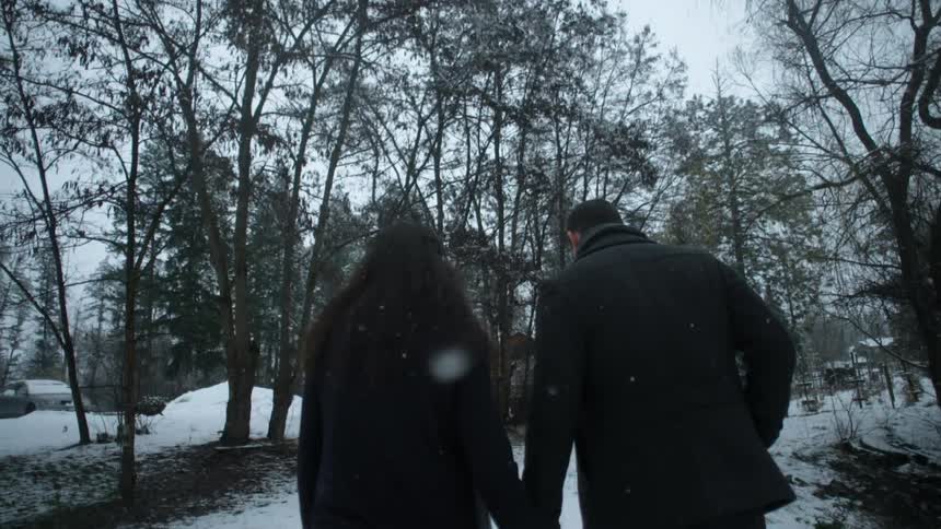 Man and woman hold hands outside while it snows
