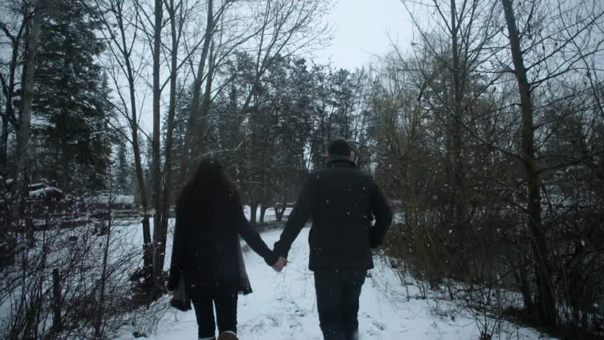 A man and women walk outside holding hands as it snows