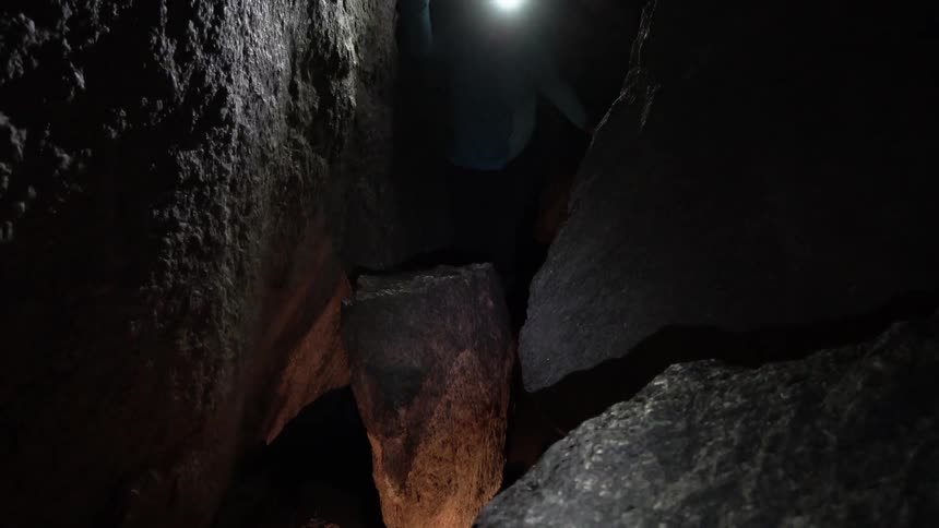 A person holding a flashlight climbs into a rocky crevice