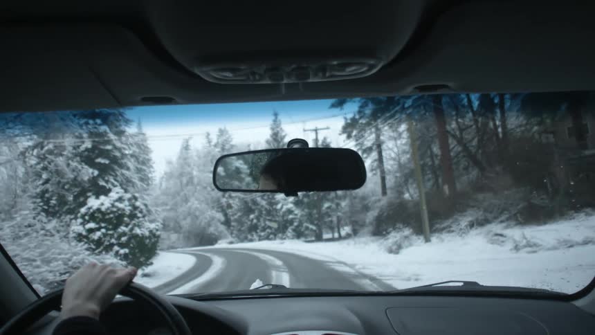 A woman is driving down a snow covered road