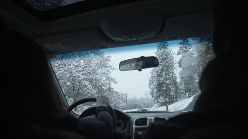 Two people are in a car driving as snow falls