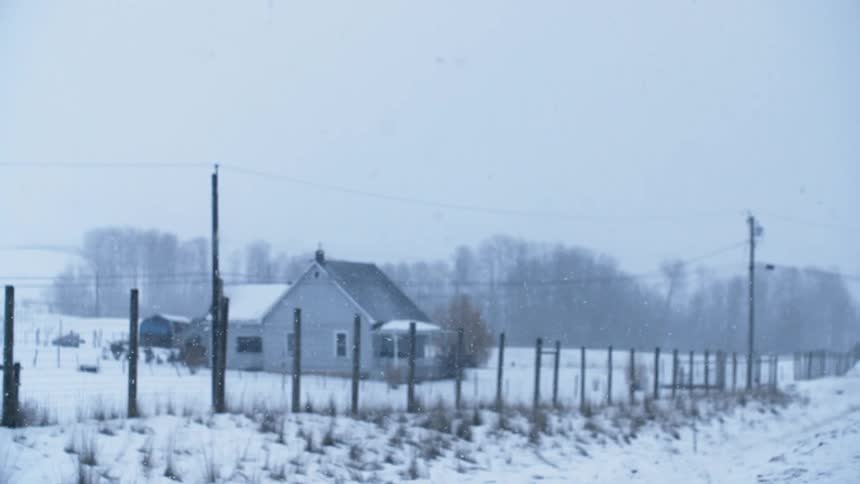 Snow falling in a rural area with a single house