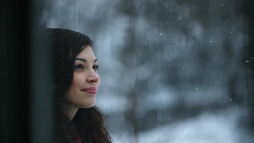 A woman stands outside smiling as the snow falls