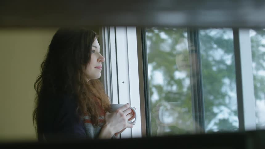 A woman is holding a mug as she looks out a window