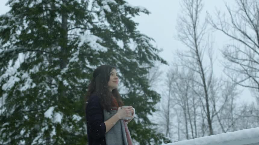 A woman is standing outside with a mug as it snows