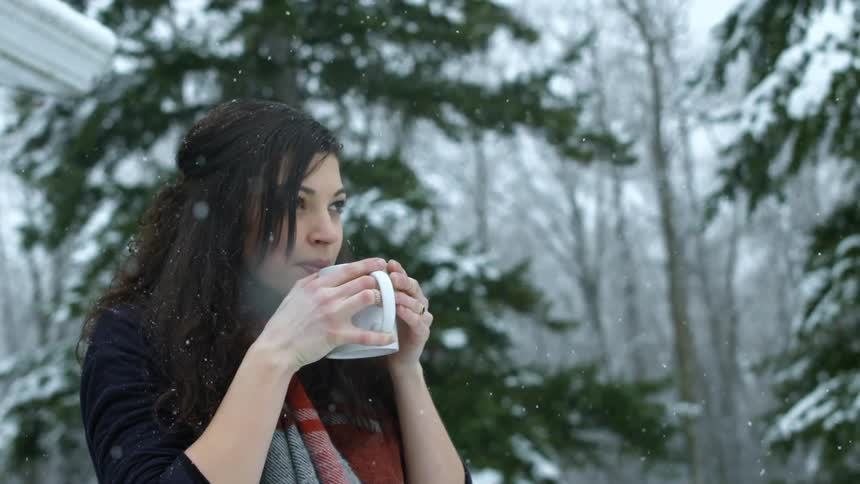 A woman drinks from a mug outside as it snows