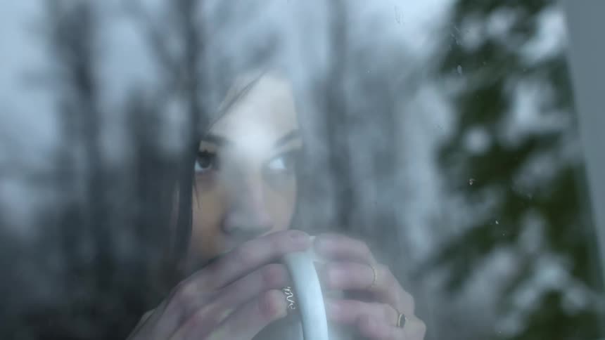 A woman drinks from a mug while looking out a window