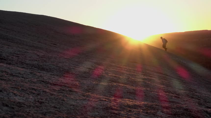 A man hikes up a hill at sunrise