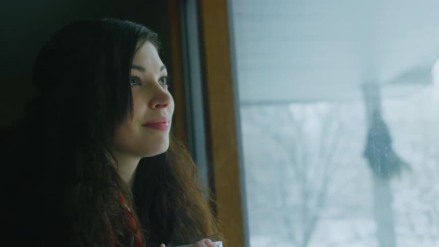A woman smiles while she looks out a window on a snowy day