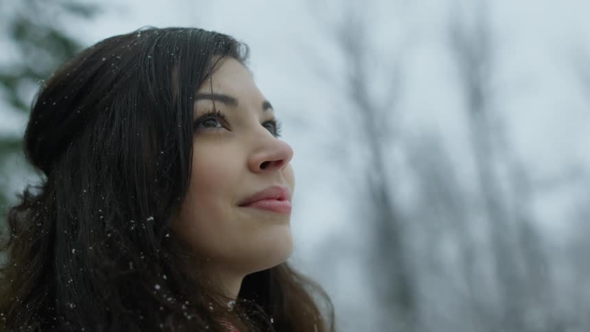 Close-up of a brunette woman standing outside watching the snow lightly fall