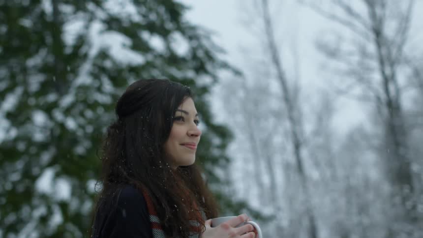 A woman is smiling as she holds a mug in the snow