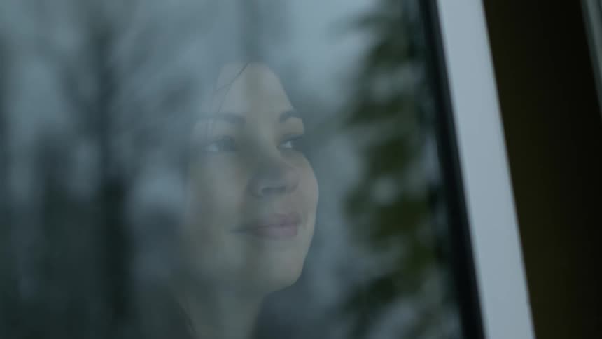 A woman is smiling as she looks out a window