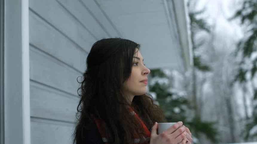 A woman exiting a home with a mug in her hands as snow falls around her