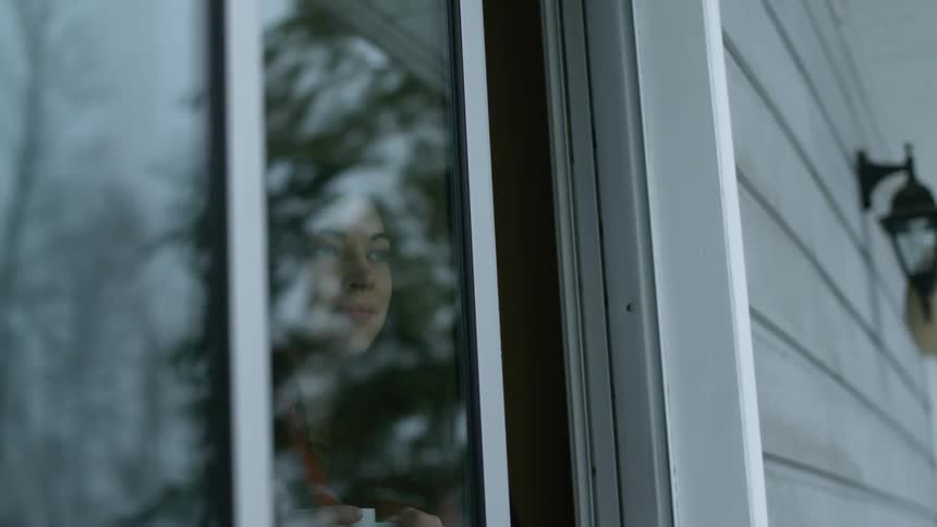 Woman holding mug standing and smiling as she looks out a window