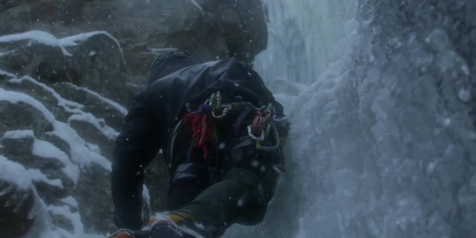 A man is climbing up the ice with ropes hanging from his belt
