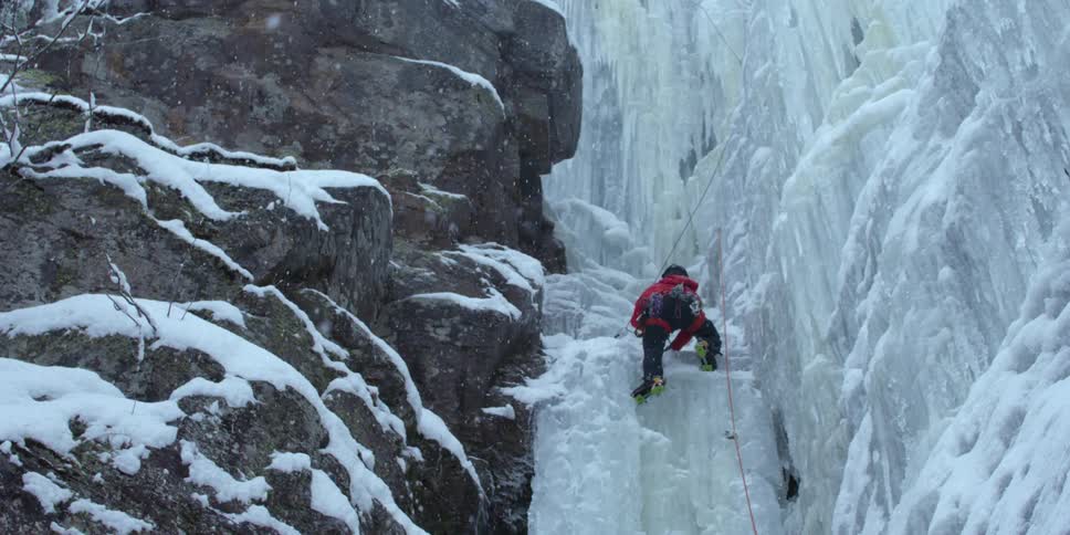 A rock climber slowly climbs over the ice as it snows