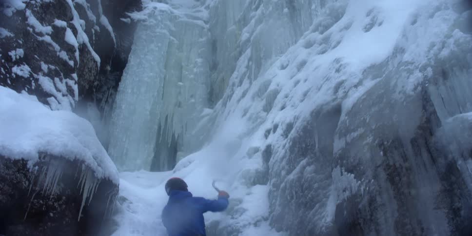Person uses hook to climb up a snow covered cliff