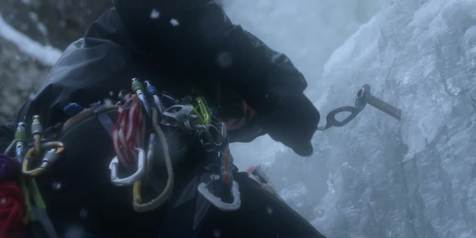 A person climbing a wall of ice is removing an anchor from the wall