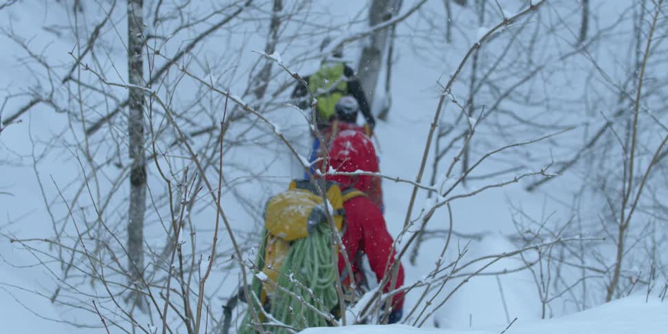People wearing backpacks hike through the snow