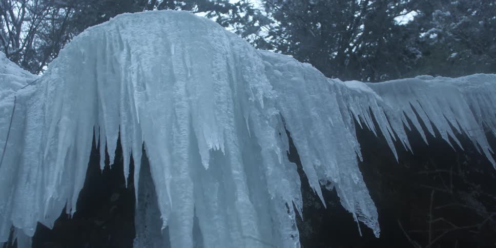 Sheets of ice hang from a rock ledge in a natural setting on a winter day