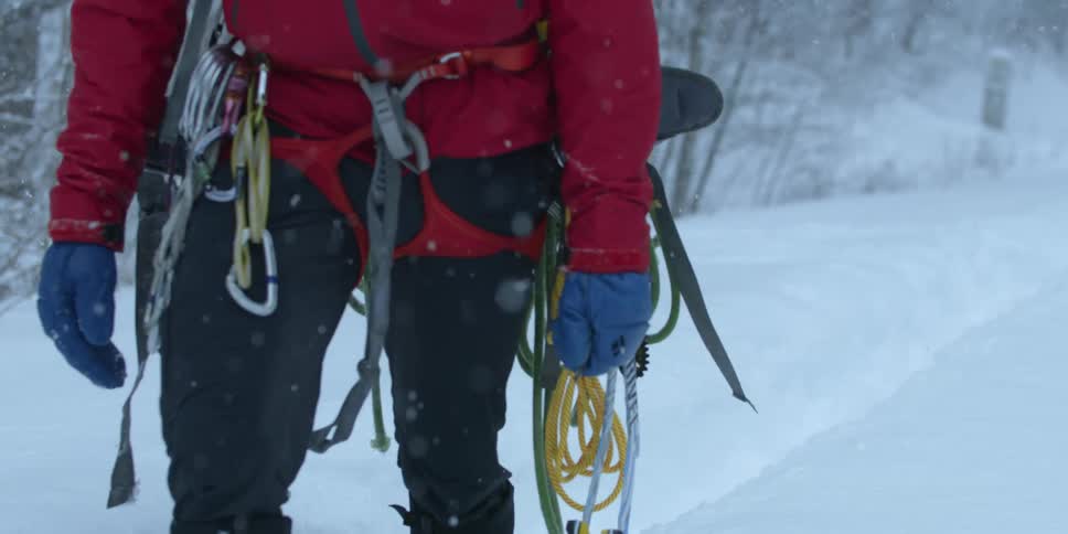 A man is hiking in the snow carrying climbing gear