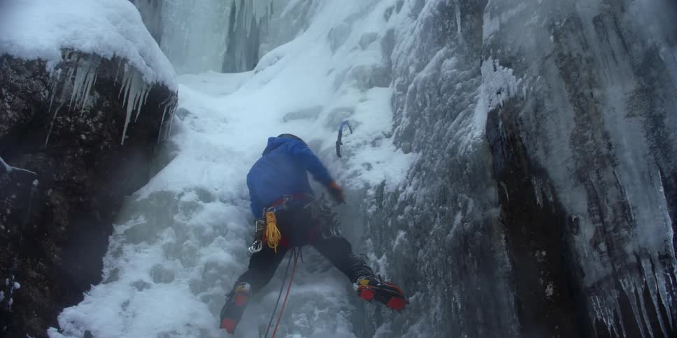 A man is climbing the ice on the side of a mountain
