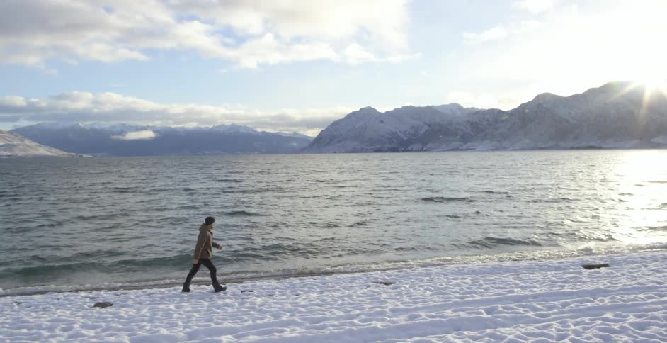 A man walking on snow next to a mountain lake