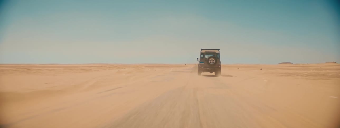 A pair of people travel across a desert in a jeep during the day