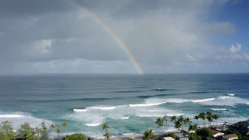An aerial daytime view of a tropical beach with homes nearby and a rainbow in the background