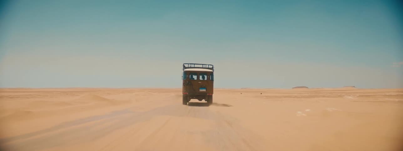 A jeep is traveling sand in a desert flatland wilderness on a sunny day
