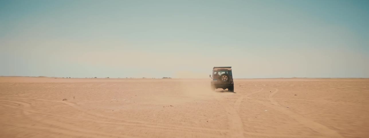 A truck travels across a desert as sand flies from behind the wheels