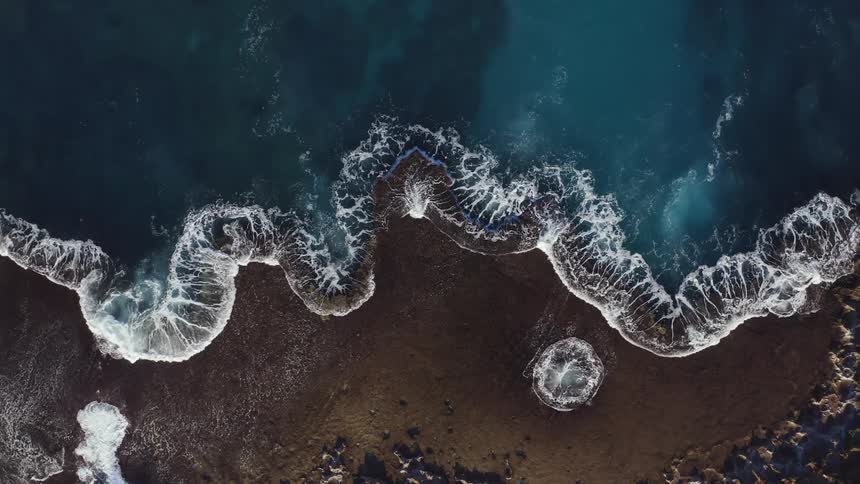 An top down aerial view of a beach with rocks during the day