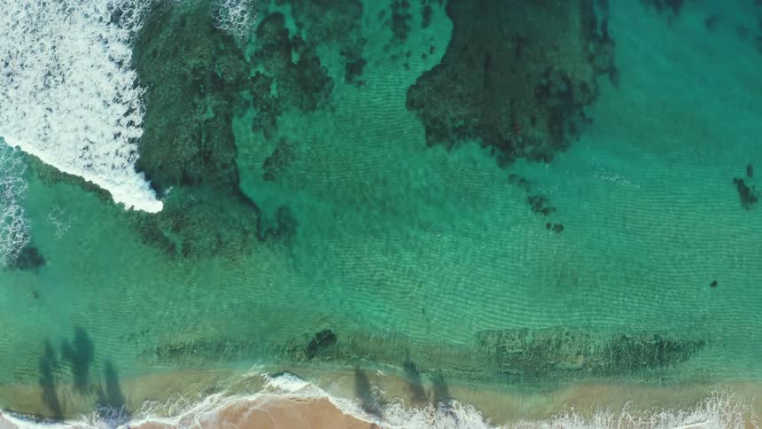 Waves roll over a beach and the water is very clear